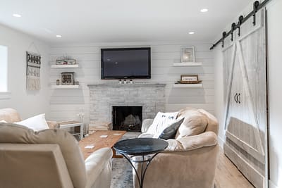 a living room featuring white walls, a stone fireplace, floating shelves, a mounted flat-screen TV, and a rustic sliding barn door