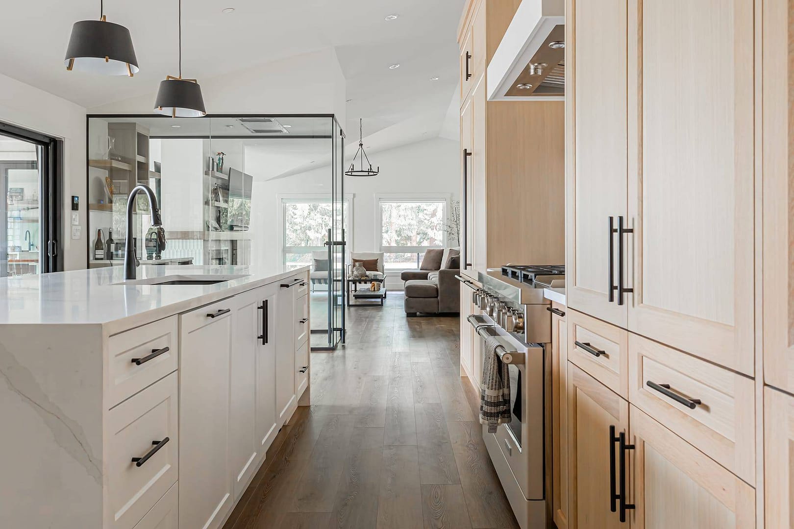 A modern farmhouse kitchen with white cabinets, and a glass wall separating it from the living room by design-build contractors in Langley