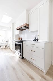 Bright white kitchen with shaker cabinets, a wood range hood, and light wood floors by Bowline Construction kitchen renovation contractor in Langley, BC