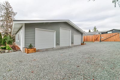 A large, detached outbuilding garage with three car bays and a gravel driveway made by by Bowline Construction in Langley, BC