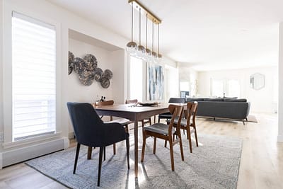 Dining room with a wooden table and six chairs, a modern chandelier, and a gray rug, connected to a living room by Bowline Construction design-build contractors in Langley, BC