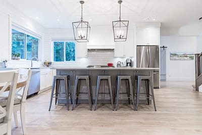 A bright and airy kitchen with white cabinets, a large island with gray bar stools, and pendant lights hanging above by kitchen renovation contractor in Langley