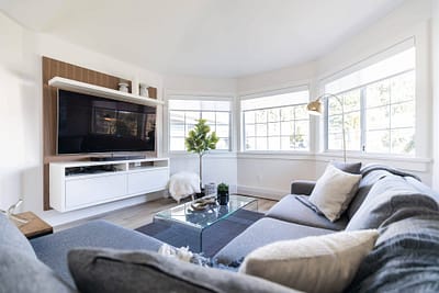 Living room with a large TV mounted on the wall, a gray sofa, and a glass coffee table by Bowline Construction home renovation contractors in Langley, BC