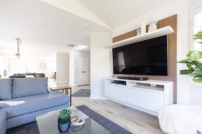 Living room with a large TV mounted on the wall, a gray sofa, and a glass coffee table by Bowline Construction home renovation contractors in Langley, BC