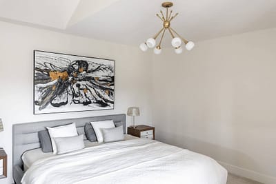 Bedroom with a gray upholstered bed, a large floral painting, and a modern chandelier in Langley, BC