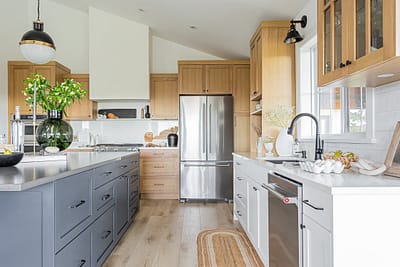 A modern kitchen with light wood cabinets, a large island with dark gray cabinets, and stainless steel appliances by Modern kitchen contractors in Langley