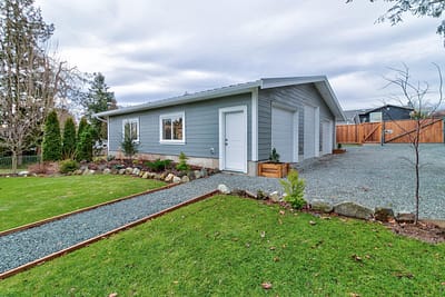 A detached, single-story building with a gray exterior, multiple windows, and a white door by home renovation contractors in Langley, BC