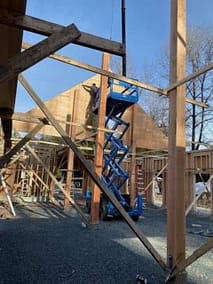 An outbuilding under construction with a scissor lift and a worker on the roof in Langley, BC