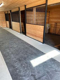 A long, well-lit barn aisle with horse stalls on either side by pole barn construction contractors in Langley, BC
