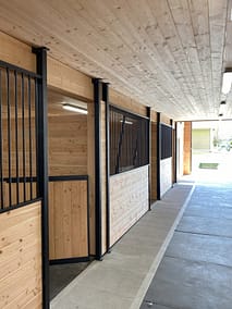 A long, well-lit barn aisle with horse stalls on either side by pole barn construction contractors in Langley, BC