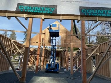 A pole barn under construction with a scissor lift in the center and the words "Country Timber" written across the top by Bowline Construction in Langley, BC.