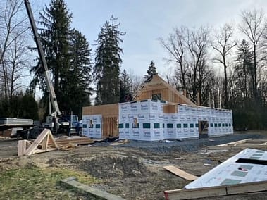 A pole barn under construction with a crane and workers on site, partially framed and covered in Tyvek house wrap by Bowline Construction in Langley, BC