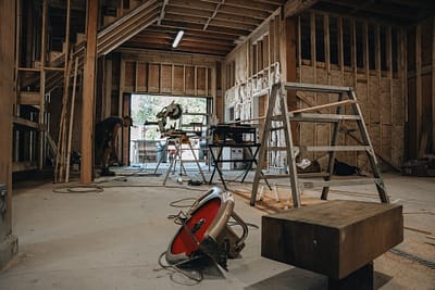 An outbuilding under construction with tools and materials scattered around. There is a miter saw, a table saw, a circular saw, and ladders visible in Langley, BC