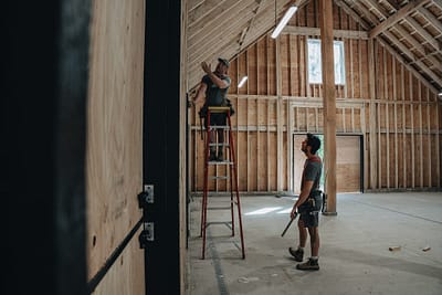 Bowline Construction team members on a ladder holding a measuring tape for pole barn construction in Langley, BC