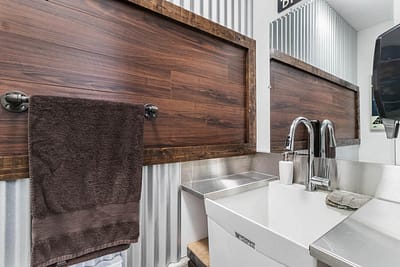 A custom additions modern bathroom with a white sink, a brown towel hanging on a rack, and a wooden panel behind it by Bowline Construction in Langley, BC