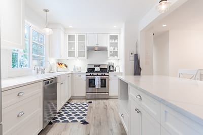 A bright, narrow kitchen with white cabinets and light wood laminate flooring.
