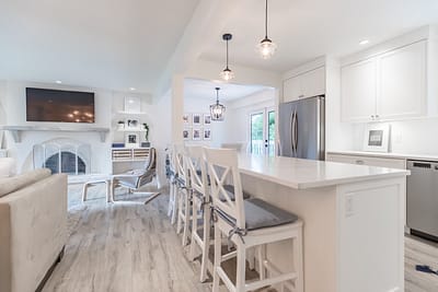 A bright, open-plan kitchen and living area with white walls and light wood laminate flooring.