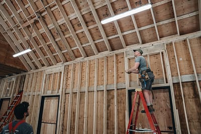 Bowline Construction team member on a ladder holding a measuring tape for pole barn construction in Langley, BC