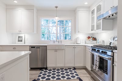 A bright, narrow kitchen with white cabinets and light wood laminate flooring.