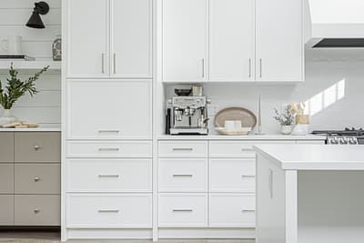 A close-up shot of a modern kitchen featuring white shaker-style cabinets and drawers with silver handles.