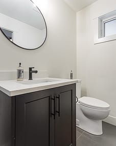 A bathroom with a dark vanity and a round mirror