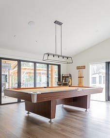 A game room with a pool table, a hanging light fixture, and sliding glass doors.
