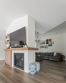 A living room with a TV mounted above a fireplace, a gray sectional sofa, and light wood floors