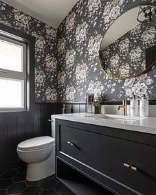A bathroom vanity with a white quartz countertop, a gold faucet, a round mirror, and a floral wallpaper