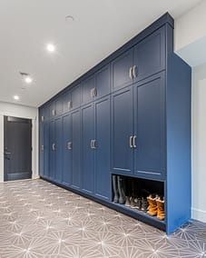 A spacious mudroom or hallway featuring a long wall of dark blue built-in cabinets with gold handles.