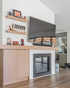 A room with a TV mounted above a fireplace, wooden shelves, a cabinet, and a partial view of a pool table