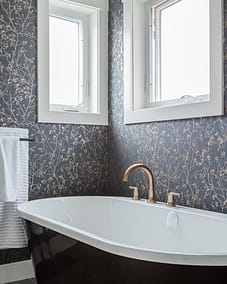 A bathroom with floral wallpaper, a black and white bathtub, two windows, and a gold faucet by home renovation contractors in Langley