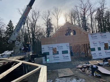 A pole barn under construction with a crane and workers on site, partially framed and covered in Tyvek house wrap by Bowline Construction in Langley, BC