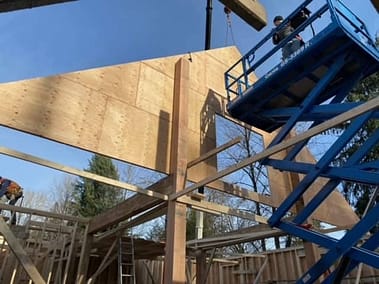 A pole barn under construction with a crane lifting a large piece of plywood into place by Bowline Construction in Langley, BC