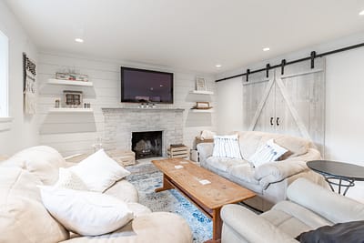 A bright living room with white shiplap walls, a painted brick fireplace, a mounted TV, and a sliding barn door with black hardware custom additions in Langley, BC