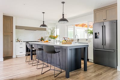 A modern kitchen with a dark gray island, gray cabinets, stainless steel refrigerator, and black pendant lights custom additions in Langley, BC