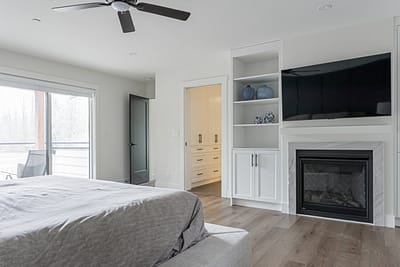 Custom additions featuring built-in cabinets, a fireplace, a mounted TV, and a ceiling fan in a modern bedroom in Langley.