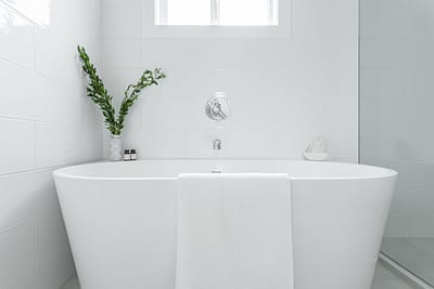 A white bathroom with an oval freestanding bathtub, white tile walls, and a glass shower door