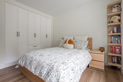 A bedroom with a bed, a white closet, a nightstand, and a bookshelf.