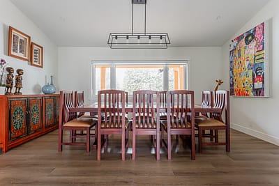 A dining room with a wooden table, chairs, a hanging light fixture, and artwork on the wall