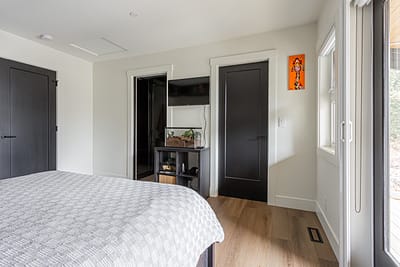 A bright, modern bedroom with white walls and light wood laminate flooring.