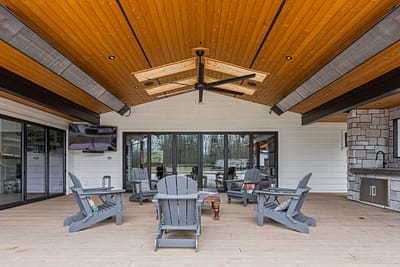 An outdoor covered patio with wood ceiling, stone fireplace, and Leisure Line Recycled Plastic Folding Adirondack Chairs.