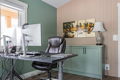 A home office with a desk, dual monitors, a chair, built-in cabinets, and a window