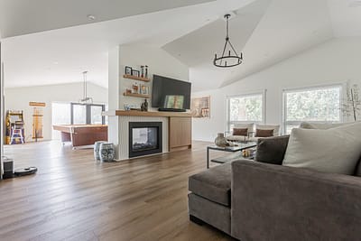 A living room with a gray sectional sofa, two armchairs, a glass coffee table, framed art on the wall, and light wood floors.