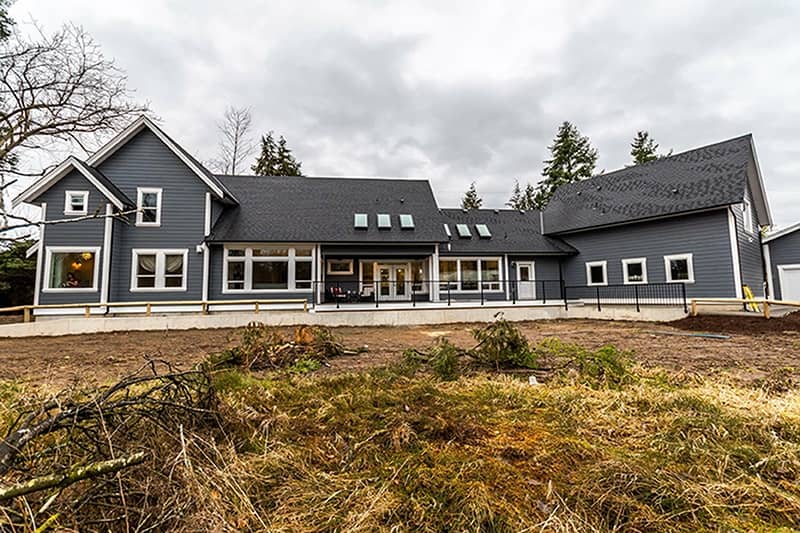 A barn with a striking black exterior paint, set against a backdrop of lush green grass and overcast grey skies, representing the rugged beauty of agricultural buildings in Langley, BC
