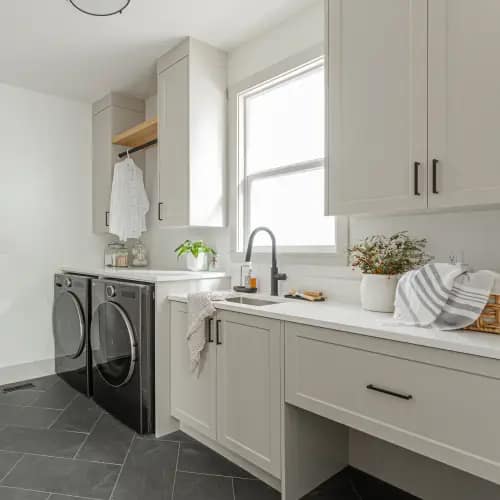 Modern laundry room renovation with white cabinetry, black washer and dryer, and natural light by Bowline Construction in Langley, BC