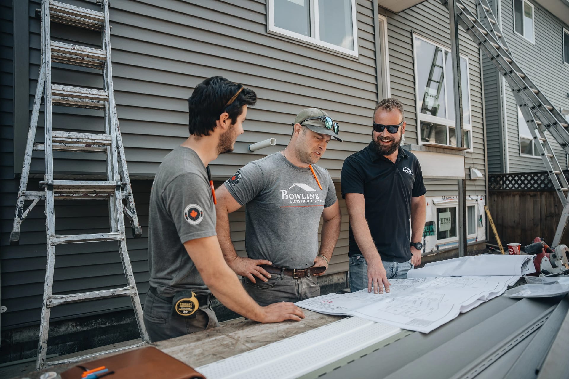 Bowline Construction design-build experts collaborating over plans in Langley, BC Bowline Construction team members discuss renovation blueprints outside a Langley, BC home during a design-build walkthrough